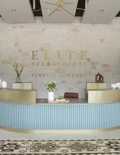 Front view of fluted teal reception desk with stone wall signage for Elite Dermatology & Plastic Surgery. Front view of fluted teal reception desk with stone wall signage for Elite Dermatology & Plastic Surgery.
