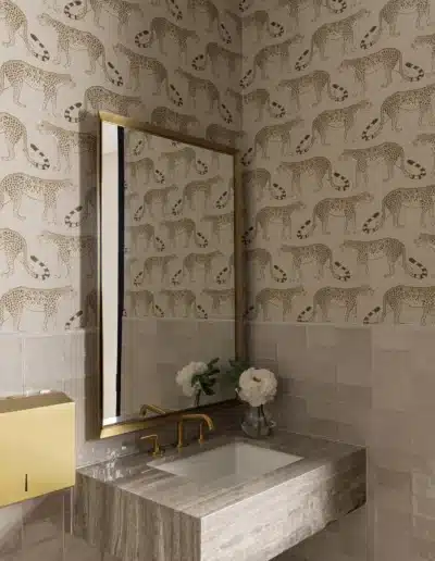 Luxury patient restroom featuring marble vanity, brass fixtures, mirror, and cheetah print wallpaper. Luxury patient restroom featuring marble vanity, brass fixtures, mirror, and cheetah print wallpaper.