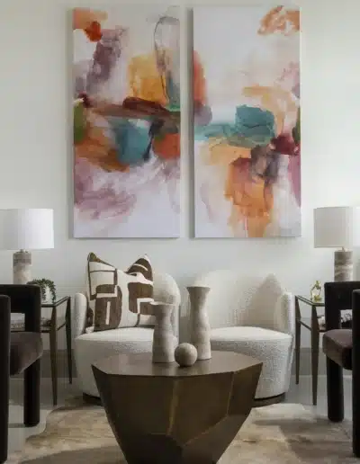 Cream boucle armchairs and geometric bronze coffee table underneath abstract paired canvas paintings. Cream boucle armchairs and geometric bronze coffee table underneath abstract paired canvas paintings.