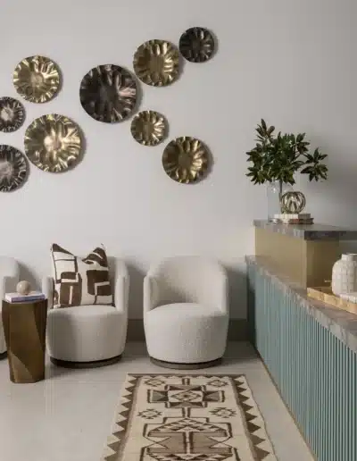 Patient waiting lounge with cream chairs, patterned runner rug, and metallic wall sculptures. Patient waiting lounge with cream chairs, patterned runner rug, and metallic wall sculptures.